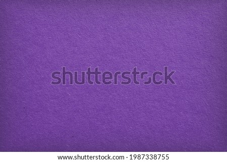The surface of violet cardboard. Paper texture with cellulose fibers. Bright purple tinted background with vignetting. Dark summer paperboard wallpaper. Saturated color. Top-down. Macro