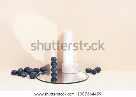 Product photography with berries and shadows. White cosmetic tube on beige background, lights, and shadows with mirror. Minimal still life.