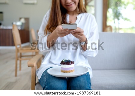 Closeup image of a young woman using mobile phone to take a photo of a cake before eat in cafe