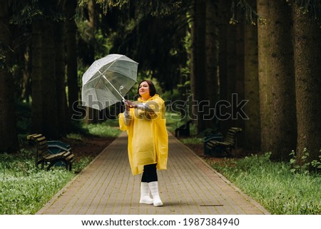 a woman in a yellow raincoat and an umbrella walks in the park and garden in summer.