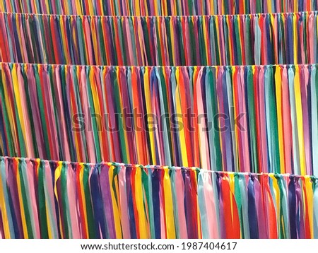 Pictures of ribbons of various colors, such as red, blue, orange, yellow, green, are hung together as a curtain.