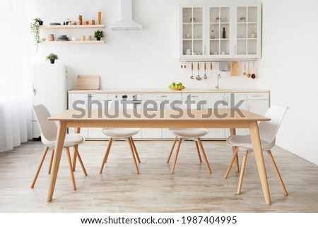 Scandinavian classic white kitchen with wooden details, minimalistic interior design. Modern furniture with accessories and various utensils, table and chairs in dinning room, copy space Royalty-Free Stock Photo #1987404995