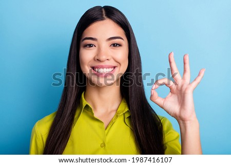 Photo of young girl happy positive smile show fingers okay sign alright deal cool ad isolated over blue color background