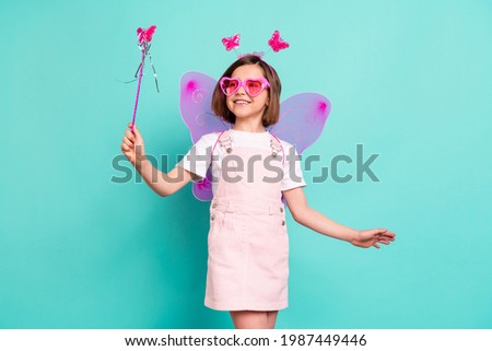 Photo of pretty adorable school girl wear pink overall glasses wings smiling holding magic wand isolated teal color background