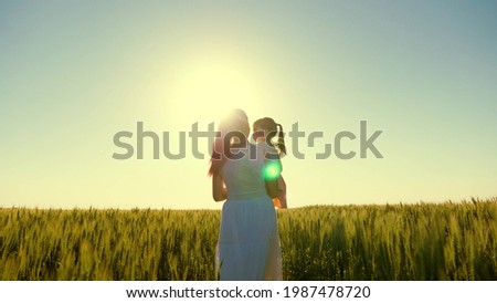 Kid and mother are walking in wheat field. Baby is in arms of mother. Mother, child, daughter are walking in green wheat field, hugging and kissing. Happy family trip. Farmer woman and child in field