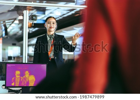 Airline attendant assisting travelers going through thermal scanning checkpoints at departure gate. Thermal body scanning of passengers before boarding their plane at the airport. Royalty-Free Stock Photo #1987479899