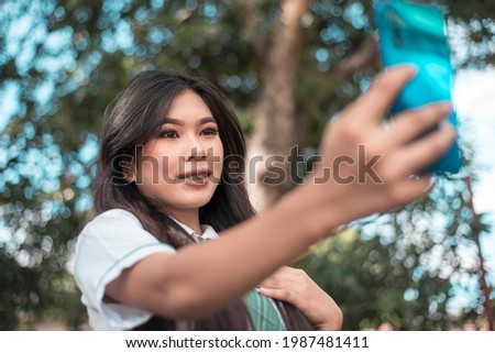 A pretty vain young asian woman in a student uniform takes a selfie of herself while at the park. Taking a photo for social media.