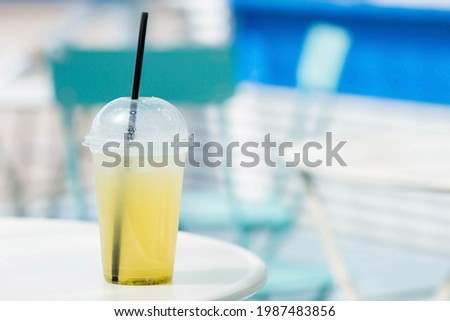 On the table in a cozy cafe is a lemonade, a plastic glass. Cooling drink with lemon and mint. Light blue-white background.