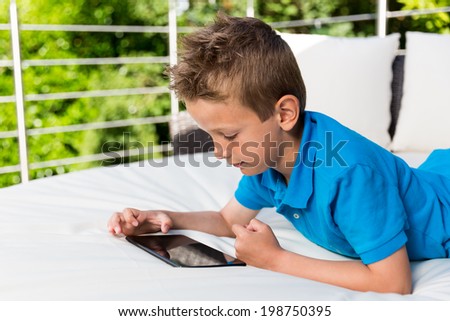 Young caucasian boy having fun with his tablet outside on the patio.