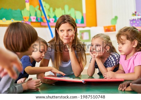 Childminder or kindergarten teacher and children read and play together in kindergarten