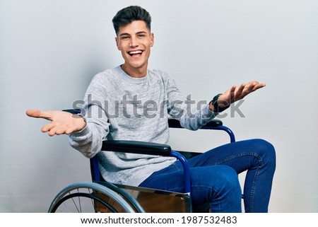 Young hispanic man sitting on wheelchair smiling cheerful offering hands giving assistance and acceptance. 