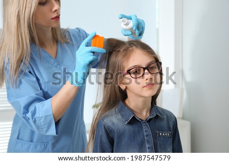 Doctor using nit comb and spray on girl's hair indoors. Anti lice treatment