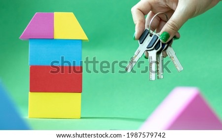 colored house from children's soft constructor on green and female hand with house keys. copy space