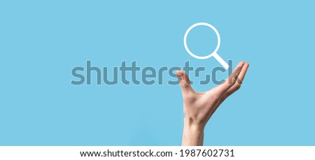 Male hand holding magnifying glass ,search icon on blue background. Concept search engine optimization, customer support.Browsing Internet Data Information.Networking Concept