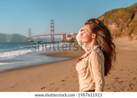  Beautiful young woman with long hair walks on the beach overlooking the Golden Gate Bridge in San Francisco