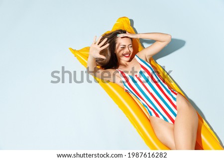 Top view young woman slim body wear striped one-piece swimsuit lies on inflatable mattress hotel pool cloced by hand isolated on pastel blue color background. Summer vacation sea rest sun tan concept