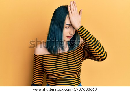 Young modern girl wearing casual striped shirt surprised with hand on head for mistake, remember error. forgot, bad memory concept. 