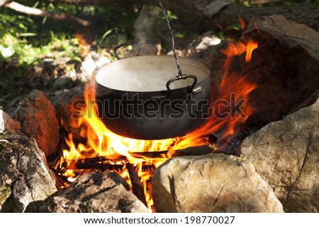 Pot water on the fire, tourists kettle on hot campfire. Camping photo.