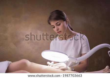 Female legs on purple sheet during epilation by a professional beautician in gloves. Spa, beauty industry, treatment at clinic, electrolysis.