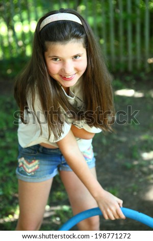 pretty preteen girl with hula hoop playing in green garden