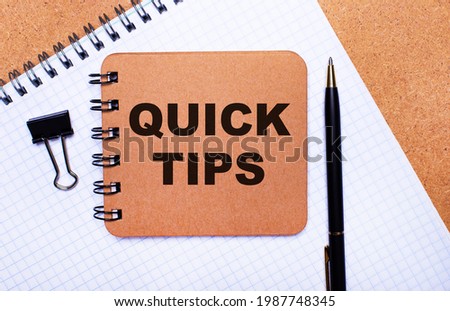 On a wooden background notepad, black pen, paper clip and brown notepad with the text QUICK TIPS. Business concept