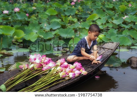 Vietnamese boy playing with pink lotus leaf when his mom boating the traditional wooden boat in the big lake at thap muoi, dong thap province, vietnam, culture and life concept Royalty-Free Stock Photo #1987754738