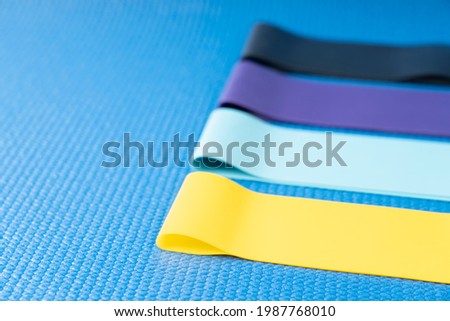 A set of colorful elastic fitness land. Expanders for women and weight loss on a blue background Flat layer of various fitness bands, space for text Elastic elastic bands for fitness, selective focus