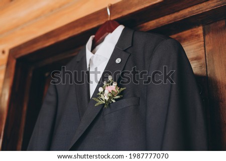 A jacket for the groom. A bow tie and a white shirt hang on a hanger. Details of the groom's wedding invitation.