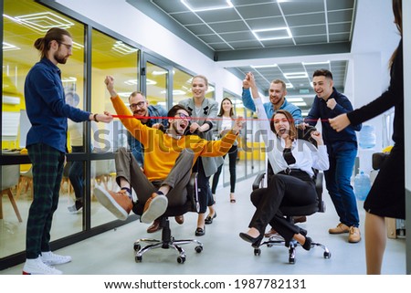 Young colleagues group having fun together, riding on chairs in office, diverse excited office workers enjoying break, laughing, engaged funny activity, celebrating corporate success. Royalty-Free Stock Photo #1987782131