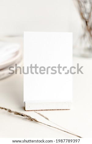 Blank white card as a table number sign mockup with minimal accessories and beige neutral colors. Earthy minimalist and modern seating card mockup for wedding stationery and events.  Royalty-Free Stock Photo #1987789397