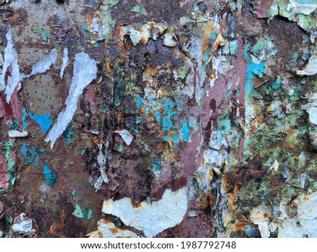 Photo of the texture of an old rusty metal wall with torn pieces of paper from ads and posters of different colors