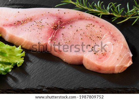 Raw Swordfish fillet covered with black pepper and with rosemary sprigs on black slate plate. Royalty-Free Stock Photo #1987809752
