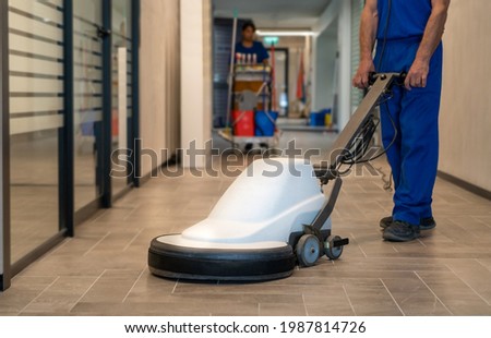Professional cleaner polish hard floor with high speed machine.Cleaning leady with trolley is in the background Royalty-Free Stock Photo #1987814726