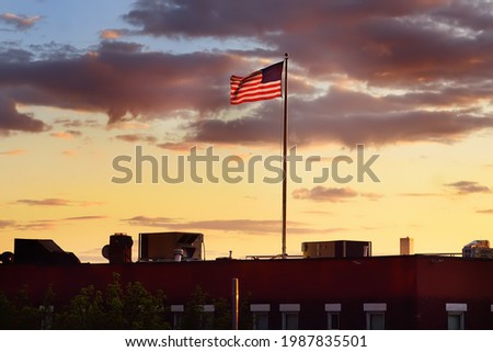 Flag of USA waving on roof top of building on background of summer sunset sky. The fourth of July is Day of Independence of United States of America.