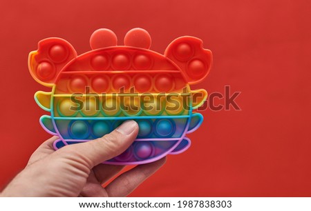a man's hand presses on a rainbow silicone anti-stress toy pop it or a simple dimple on a red background. New popular silicone colorful antistress pop it toy for child on red background. New Trend.