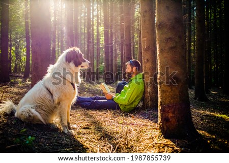 man with dog reading a book in forest