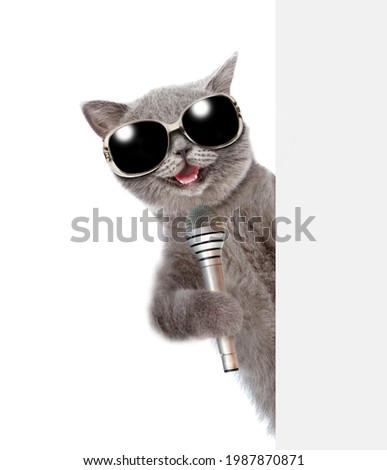 Cat wearing sunglasses holds microphone behind empty white banner. isolated on white background.