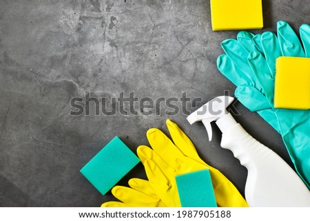 Yellow rag and yellow, green sponges, rubber gloves, cleaner spray bottle on a gray concrete background. House cleaning service and housekeeping concept. Flat lay, copy space. Cleaning supplies.