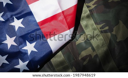 Military hat or bag laying with american flag. Soldier hat or helmet with national american flag on black background. Represent military concept by camouflage object and USA nation flag.