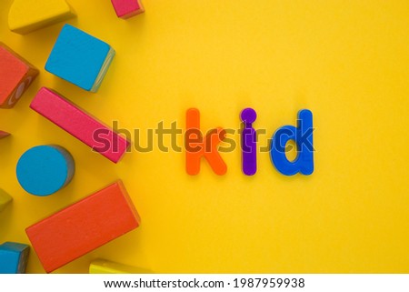 Kids Education, Creative, logical thinking concept. Colourful multicoloured building wooden toy blocks for children learning development word Kid from plastic letters on yellow background flat lay