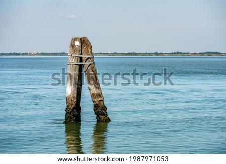 Venice lagoon with three big wooden poles implanted in the seabed called Briccola or Bricola (Dolphin), used to indicate the viable routes in the sea to boats. Veneto, Italy, Europe.