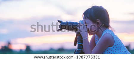 Cute little girl taking picture silhouette sunset sky by camera on tripod standing with happy