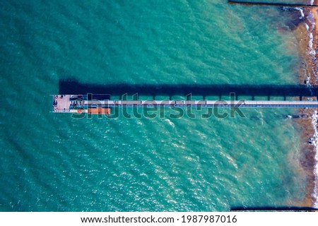 Pier against backdrop of turquoise sea with fine waves, sunny day, loneliness concept. Aerial top view.