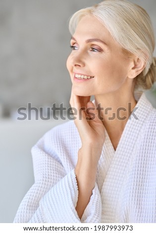 Headshot vertical portrait of smiling middle aged woman wearing bathrobe touching face at spa salon hotel looking away. Bodycare spa procedures skin care antiaging products concept. Royalty-Free Stock Photo #1987993973
