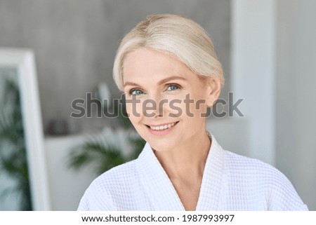 Portrait of happy smiling beautiful middle aged woman wearing bathrobe at spa salon hotel looking at camera. Advertising of bodycare spa procedures antiage delicate dry skin care products concept. Royalty-Free Stock Photo #1987993997