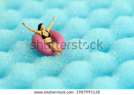 Miniature people toy figure photography. Girl wearing black sunglass swimming with rubber tube ring on wavy ocean. Image photo