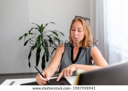 Portrait of a young female worker drawing on a tablet and working on a laptop.