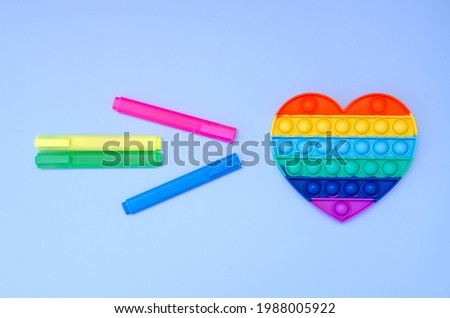 Top view of colorful markers and anti stress sensory toy pop it rainbow heart on blue background close up. Creative and funny concepts of children toys. Popular toy. Trend toy 2021 year.