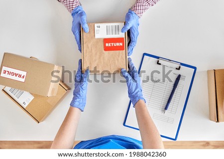 health protection, delivery and mail service concept - customer making return of parcel or purchase and worker in protective gloves receiving box Royalty-Free Stock Photo #1988042360