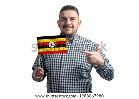 White guy holding a flag of Uganda and points the finger of the other hand at the flag isolated on a white background.